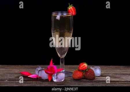 Ein vernebeltes Glas Champagner, frische Erdbeeren und Eisstücke auf dunklem Grund Stockfoto