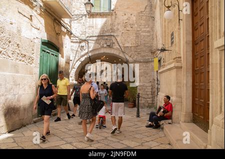 Touristen in der Altstadt von Bari im Sommer und alte Straßenmusiker spielen Akkordeon vor der Kirchentür Stockfoto