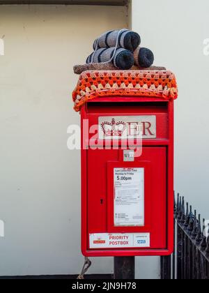 HATHERLEIGH, DEVON, ENGLAND - AUGUST 9 2022: Roter Briefkasten. Sie ist mit Häkelteerfässern auf dem Schlitten geschmückt, die Teil des jährlichen Festivals der Stadt sind. Stockfoto