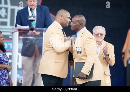 Richard Seymour, ehemaliger New England Patriots Defensive End, schüttelt sich mit Bryant Young, dem ehemaligen San Francisco 49ers Defensive End, während der Pro Football Hall of Fame Verankerungszeremonie im Tom Benson Stadium in Canton, Ohio, am 6. August 2022. Die Wähler hatten 8 Mitglieder für die PFHOF-Klasse von 2022 ausgewählt Stockfoto