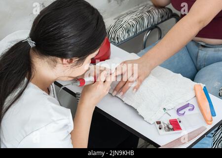 Junge Latina Manikuristin, Polieren eines Mädchens Nägel mit einem elektrischen Nagelpuffer, Lernen der Kunst der Maniküre. Studieren und üben Nageldesign und Stockfoto