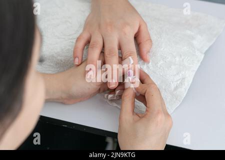 latina Manikuristin reinigt die Nägel eines Mädchens mit einem Wattestäbchen und bereitet sie auf den Arbeitsbeginn vor. Detail der Hände einer Frau, die Nagellack von einem gi entfernt Stockfoto