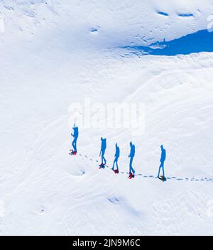 Eine Gruppe von Wanderern aus der Luft mit Schatten, die im Schnee in einer Reihe zu laufen scheinen Stockfoto