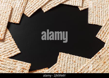 Ein Foto von Matza oder Matza-Stücken auf schwarzem Hintergrund. Matza für die jüdischen Passahfeiertage. Platz für Text, Platz zum Kopieren Stockfoto