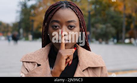 Nahaufnahme junge selbstbewusste geheimnisvolle afroamerikanische Frau, die draußen steht und Schweigen zeigt Geste zeigt, Finger in den Mund legt, verbietet das Sprechen Stockfoto