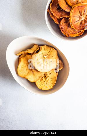Schüsseln mit Apfel- und Kaki-Chips auf Betontisch Stockfoto