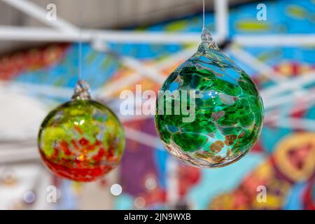 Bunte hängende Glaskugeln mit selektivem Fokus auf die grüne Kugel im Vordergrund. Zu den Konzepten gehören Kunst, Dekor, Urlaub, andere. Stockfoto