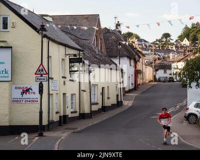 HATHERLEIGH, DEVON, ENGLAND - AUGUST 9 2022: Blick entlang der Bridge St mit Hütten, Fahnen und einem jungen Mann auf einem Skateboard, Stockfoto