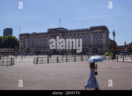 London, Großbritannien. 10.. August 2022. Eine Frau, die sich mit einem Sonnenschirm vor der Sonne schützt, geht an einem sengenden Tag am Buckingham Palace vorbei, da die Hitzewellen und Dürren, die durch den Klimawandel verursacht werden, in Großbritannien anhalten. Kredit: Vuk Valcic/Alamy Live Nachrichten Stockfoto