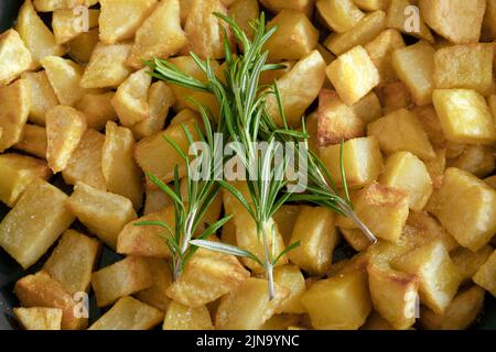 Makro-Nahaufnahme eines Rosmarinzweiges mit hausgemachten Bratkartoffeln im Hintergrund. Stockfoto