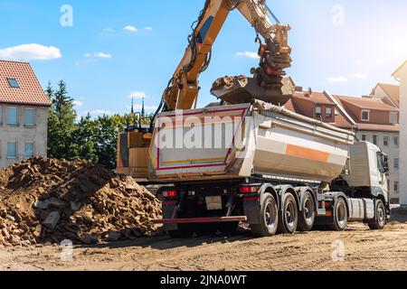 Schwere Baggermaschine Upload von Abfall und Schutt Schutt in Muldenkipper auf der Baustelle. Abbau von Gebäuden und Entsorgung von Bauabfällen Stockfoto