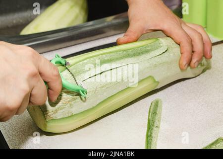 Rezept für Zucchini-Krapfen. Schritt 1 - die Zucchini schälen. Die Hände schälen grüne Zucchini mit einem Gemüseschäler. Stockfoto