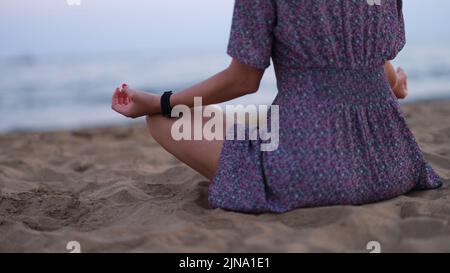 Eine kurze Aufnahme einer unerkennbaren jungen Frau, die am Strand meditiert Stockfoto