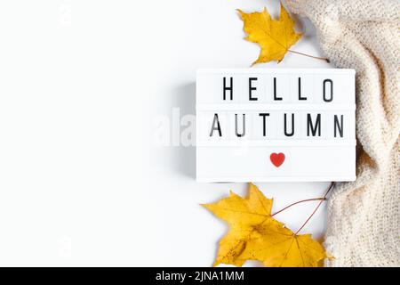 Hallo Herbst. Schild mit Aufschrift, Strickpullover und gefallenen Blättern auf weißem Grund. Beginn der Herbstsaison. Flach liegend, Kopierplatz. Stockfoto