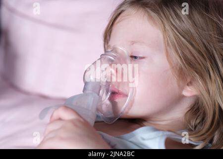 Krankes Mädchen in Sauerstoffmaske liegt auf Krankenhausbett Stockfoto