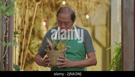 Asiatisch-amerikanischer Geschäftsinhaber eines lokalen Ladens, der Schürze trägt und die Anlage in den Händen hält. Ein glücklicher Unternehmer mittleren Alters, der vor der Kamera lächelt. Kleine Busine Stockfoto