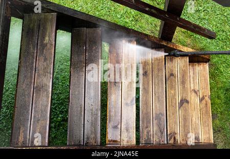 Nahaufnahme der Verwendung eines Hochdruckreinigers zur Reinigung von imprägnierten Holzterrassentreppen im Freien im Frühjahr. Vor und nach der Reinigung, großer Kontrast. Stockfoto