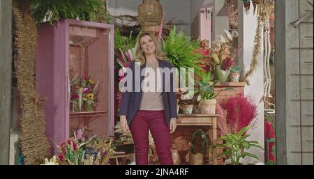 Geschäftsfrau Inhaberin eines lokalen Blumenladens, die vor dem Geschäft steht. Porträt einer Unternehmerin, die vor der Kamera lächelt Stockfoto