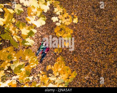 Blick von oben auf Frau mit Mann, der sich auf dem Boden mit Herbstblättern legt Stockfoto