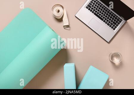 Yoga-Praxis, Meditation, Lernen und Edication. Grüne Matte, zwei Blöcke, Wasser, Uhr und weißes Armband auf beigem Hintergrund. Draufsicht. Stockfoto