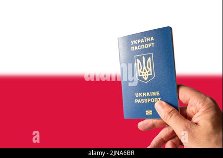 Biometrischer Pass eines Bürgers der Ukraine in der Hand einer Frau vor dem Hintergrund der polnischen Nationalflagge. Flucht aus der russischen Aggression Stockfoto