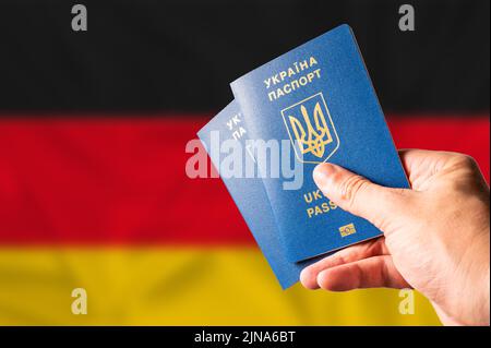 Zwei ukrainische biometrische Pässe in der Hand einer Frau vor dem Hintergrund der deutschen Nationalflagge. Reisen ukrainischer Bürger nach Deutschland, nach Stockfoto