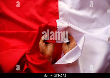 Nahaufnahme der Hände einer Person, die die rot-weiße indonesische Flagge hält Stockfoto