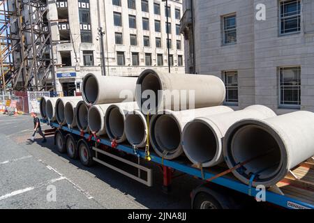 Eine große Charge von Betonabflussrohren, die auf einem Flachbettwagen auf eine Baustelle geliefert werden. Stockfoto