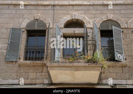 Jerusalem, Israel - 30.. April 2022: Ein typischer Balkon mit gewölbten Fenstern und Metallfensterläden in einem Steinhaus im alten Jerusalem, Israel. Stockfoto