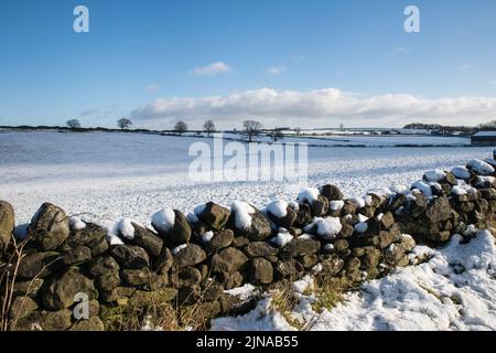 Schneebedeckte Felder und Trockensteinmauern in der Nähe des Dorfes Holloway, Derbyshire, England Stockfoto