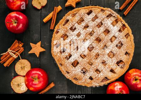 Hausgemachter Apfelkuchen mit Äpfeln, Nüssen, Zimtstangen und Herbstblättern. Thanksgiving Dinner flach legen Zusammensetzung auf einem Holztisch. Stockfoto