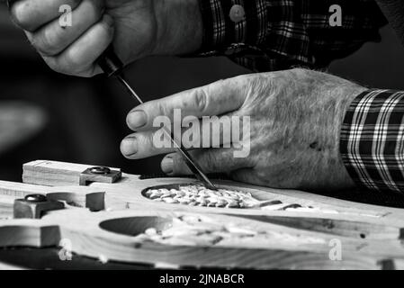 Nahaufnahme der männlichen Hände mit einer Ausgußform, um ein Muster in Holz zu schnitzen. Stockfoto