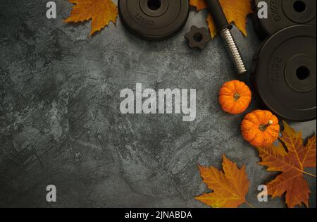 Schwere Hantelscheiben mit kleinen dekorativen Kürbissen und Herbstblättern. Gym Fitness Workout flach Lay Komposition mit Kopierer Platz. Stockfoto