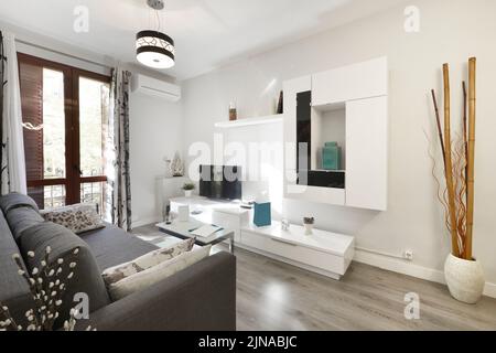 Wohnzimmer mit hellweißem dekorativem Bücherregal, Schlafsofa mit grauem Stoff und Holzfußboden Stockfoto