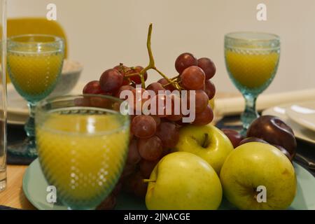 Herzstück mit Tablett mit frischem Obst, Trauben, viel Bananen, goldenen Äpfeln, reifen Pflaumen und Gläsern Orangensaft Stockfoto