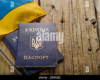 Zwei blaue biometrische ukrainische Flaggen und eine kleine ukrainische Flagge auf einem schlichten Holzhintergrund. Persönliche Identifikation, Reisen um die Welt, Patrioti Stockfoto