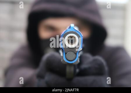 Eine Zeigekanone in den Händen eines maskierten Mannes mit schwarzer Kleidung und Handschuhen, ein kriminelles Konzept Stockfoto