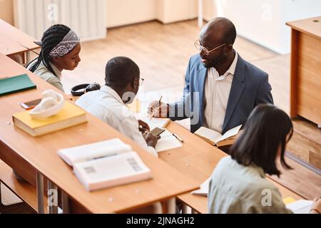 Der Lehrer gibt dem Schüler bei seiner Aufgabe Ratschläge, während er am Schreibtisch im Auditorium sitzt Stockfoto