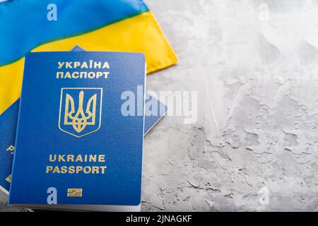 Ukrainische Staatsflagge und ukrainische biometrische Pässe auf hellem Hintergrund. Internationaler Tourismus, Reisen, Business, Freizeit, Emigration, Krieg in Ukr Stockfoto