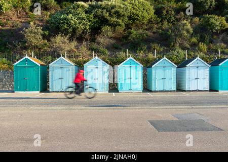 Reihe von bunten hölzernen Strandhütten am Meer in Bournemouth Dorset UK Radfahrer verschwommen Stockfoto