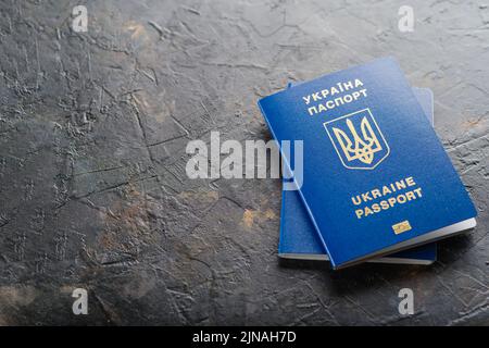 Auf einem dunkelgrauen Hintergrund befinden sich zwei ukrainische biometrische Pässe. Minimalismus. Reisen, Geschäft, Emigration, Russlands Krieg gegen die Ukraine, Flüchtlinge. Stockfoto