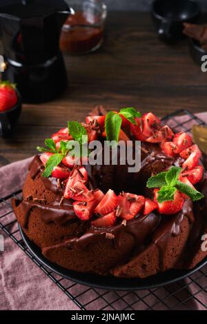 Dunkler Schokoladenkuchen mit Ganache-Vereisung und Erdbeere auf dunklem Stein- oder Betontischhintergrund. Festlicher Kuchen. Selektiver Fokus Stockfoto