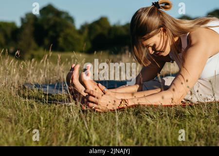 Junge Frau, die sich im Freien auf dem Gras dehnt Stockfoto