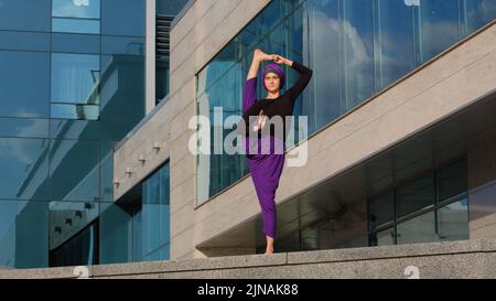 Starke muslimische Frau in Hijab Flexibles junges Mädchen dehnt Yogi Yoga Workout Baum Pose Asana weiblich hebt Bein in der Luft dabei gespaltene Strecke einen Fuß Stockfoto