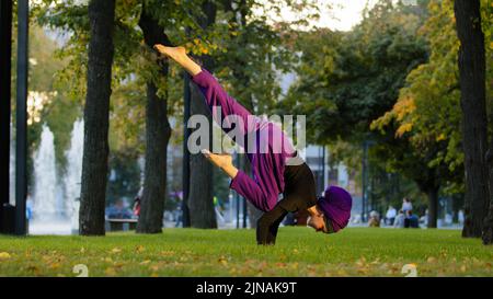 Starke aktive muslimische Mädchen in Hijab Frau Yogi Sportlerin macht Yoga-Training im Park auf grünem Rasen tun Balance Handstand Training halten Bein in der Luft Stockfoto