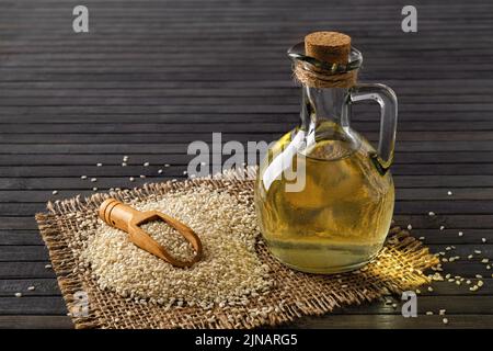 Frisches Sesamöl in einem Glaskrug und Haufen weißer bis-Samen auf schwarzem Hintergrund. Pflanzenöl aus Sesamum indicum. Bio-Benne-Samen. Stockfoto