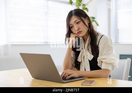 Eine beunruhigte Japanerin durch Fernarbeit im kleinen Büro Stockfoto