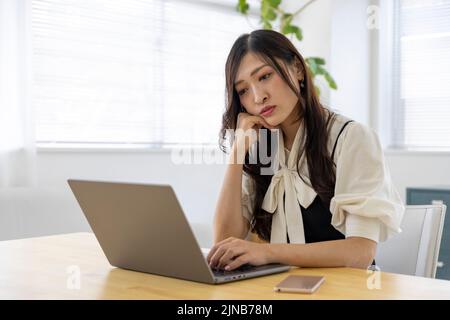 Eine beunruhigte Japanerin durch Fernarbeit im kleinen Büro Stockfoto