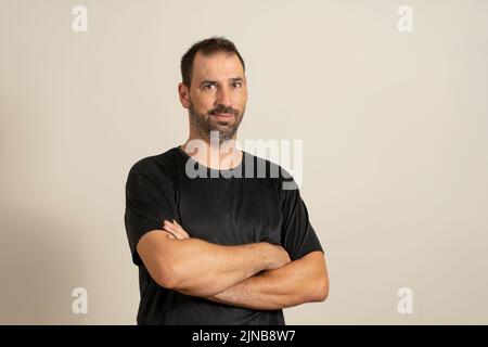Bärtiger latin-Mann posiert lustig mit gekreuzten Armen isoliert auf beigefarbenem Studiohintergrund. Stockfoto