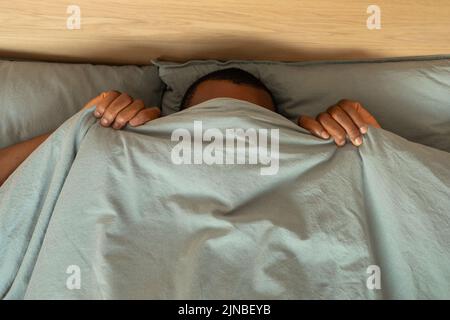 Schwarzer Mann Versteckt Das Gesicht Mit Decke Liegen Im Schlafzimmer Stockfoto